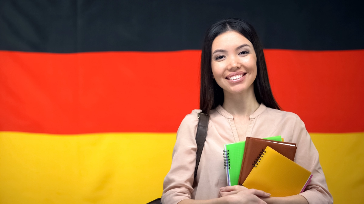 Happy female student holding copybooks against German flag background, education